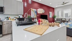 A modern kitchen with a white island, red accent wall, and pendant lighting. - The Jasper 2BD TH: 7ST Walkable, Stylish & Homey! (Fort Worth)