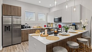 A modern kitchen with stainless steel appliances, a central island with stools, and pendant lighting. - The Quartz 2BD TH: 7ST Walkable, JOYfull & Comfy! (Fort Worth)