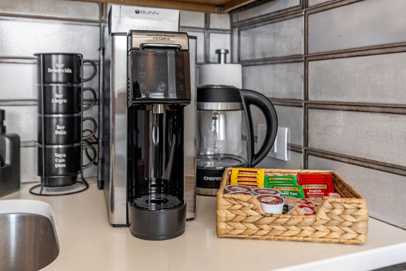 A kitchen with a Hamilton Beach Flexbrew coffee maker, a coffee maker, and a basket of Twinings tea bags.