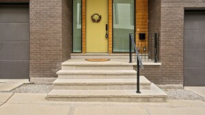 A modern building entrance with a yellow door, a small porch, and a metal railing.