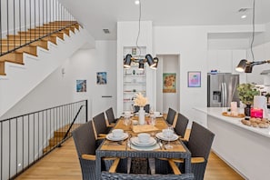 A modern dining area with a wooden table, wicker chairs, and a staircase with wooden steps.