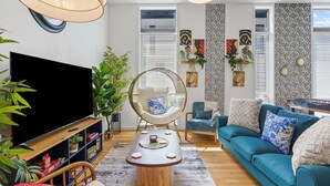 A modern living room with a flat-screen TV, a round wicker chair, a blue sofa, and a coffee table.