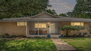 A single-story house with a front porch, a welcome sign, and a small garden area with potted plants. - Charming 2BD: TCU Walkable, Blissful & Joyful ! (Fort Worth)
