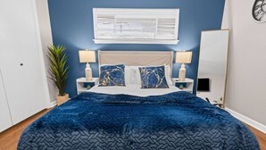 A bedroom with a bed, two bedside tables, a nightstand, a potted plant, a wall-mounted air conditioner, and a TV. - Charming 2BD: TCU Walkable, Blissful & Joyful ! (Fort Worth)