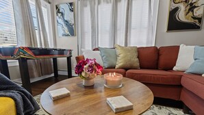 Ein Wohnzimmer mit einer Couch, einem Couchtisch mit Kerze, einer Blumenvase und einem Billardtisch.