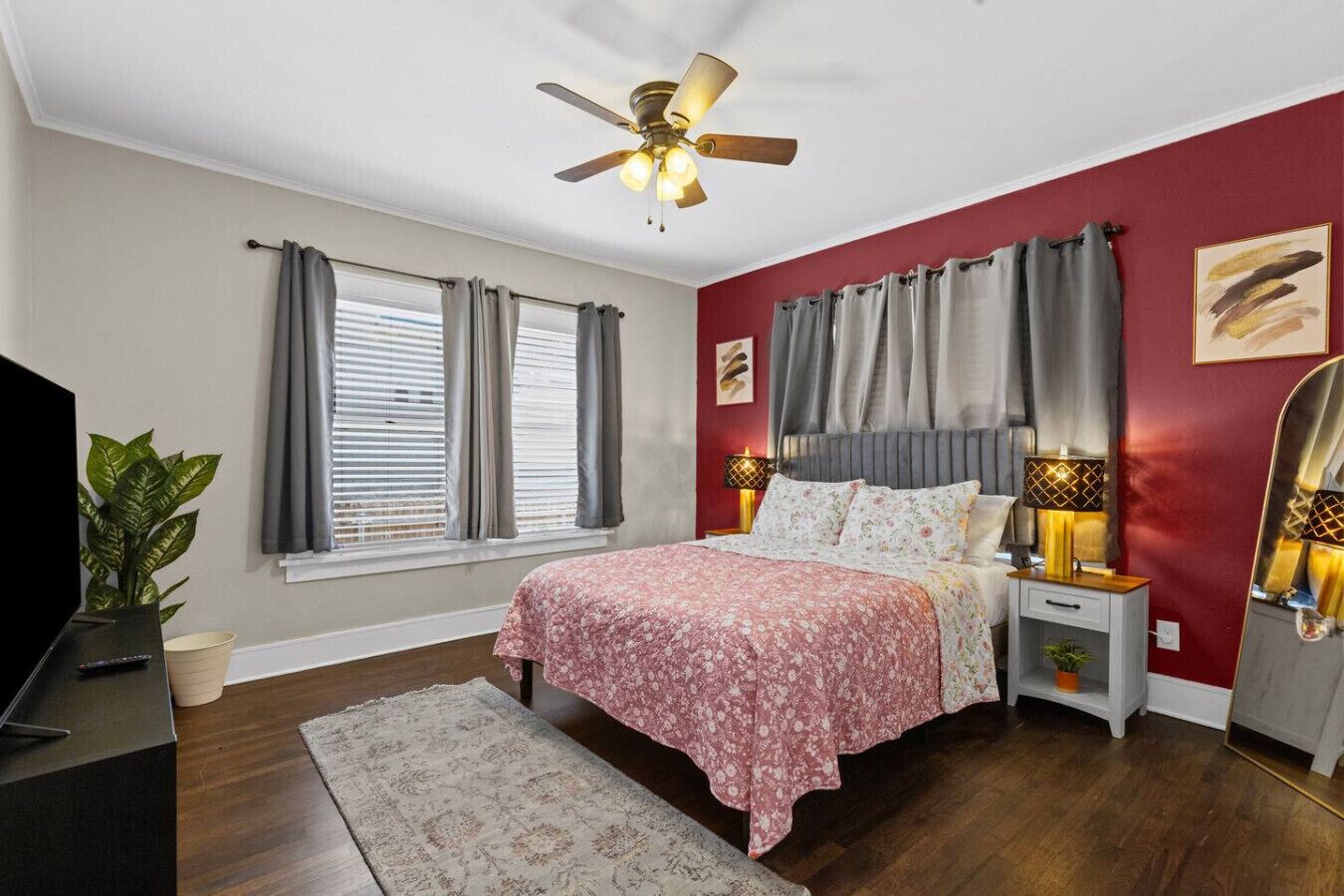 A bedroom with a bed, bedside lamps, a ceiling fan, a TV, and a plant.