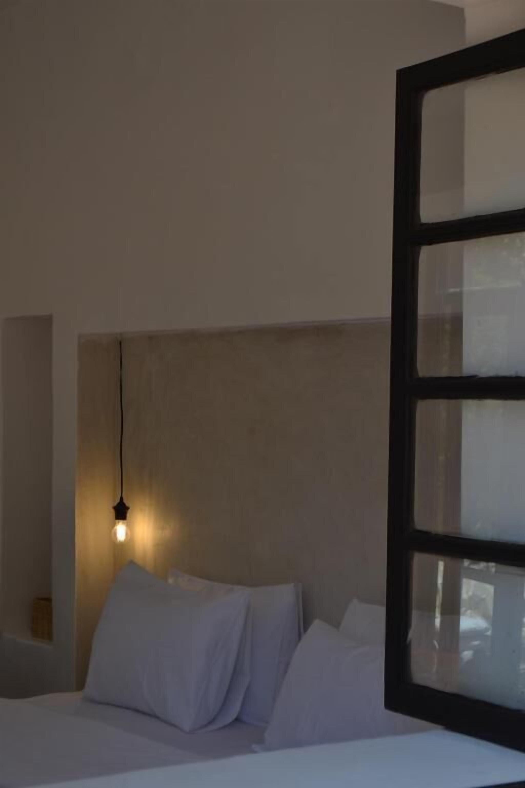 Une chambre à coucher avec un lit, des oreillers blancs, une tête de lit et un luminaire suspendu.