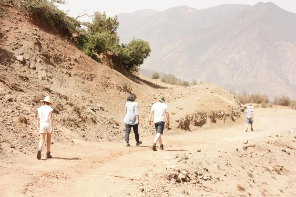 A group of people walking on a dirt road in a hilly area with sparse vegetation and mountains in the background.