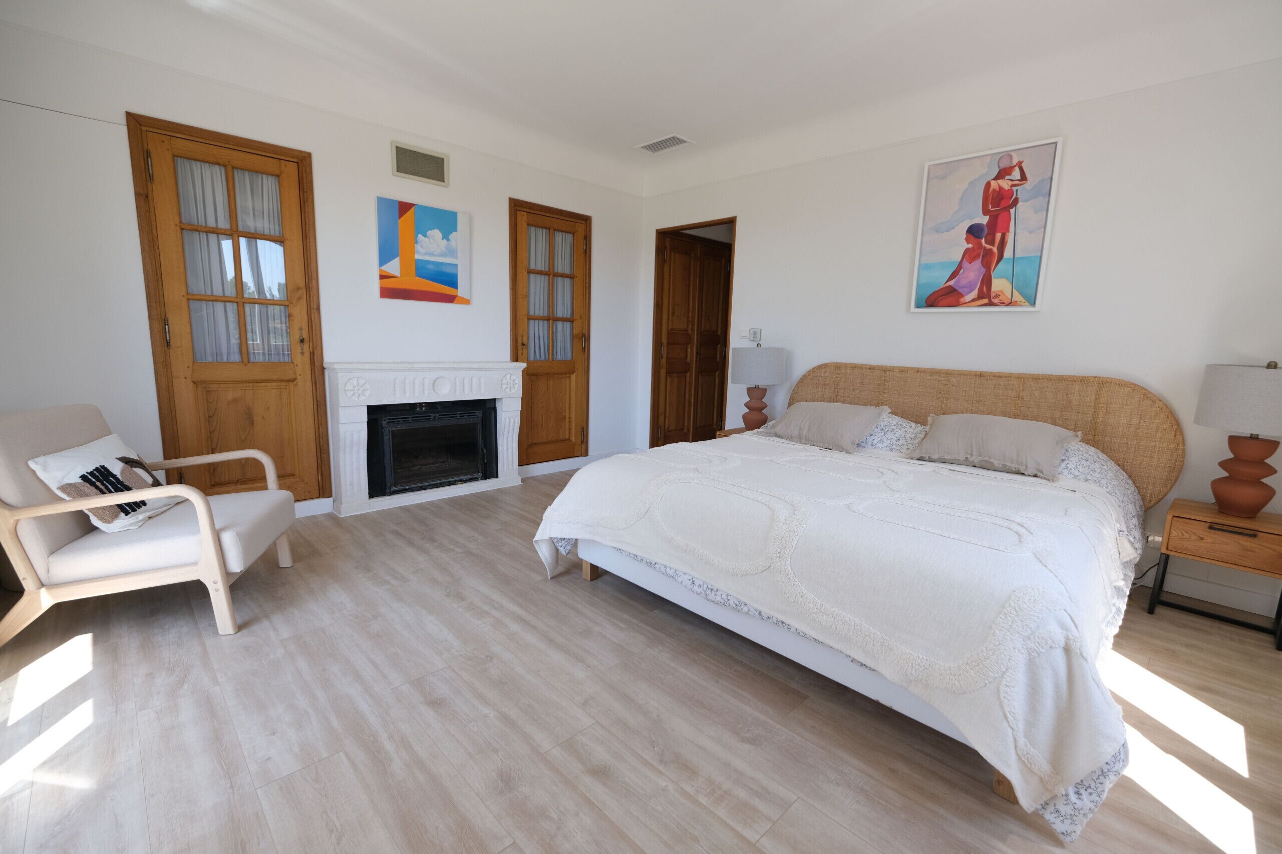 Een slaapkamer met een bed, een stoel, een open haard en kunstwerken aan de muur.