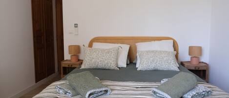 A neatly made bed with striped bedding and two folded towels. There are two bedside tables with lamps, a wooden headboard, and a door in the background.