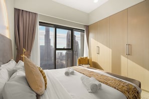 A hotel room with a large bed, a view of the cityscape, a wooden wardrobe, and a yellow armchair.