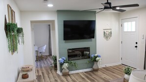 A living room with a flat-screen TV mounted on a green wall, wooden flooring, and a ceiling fan. - Delightful 2-bedroom house with AC in charming Easley (Easley)