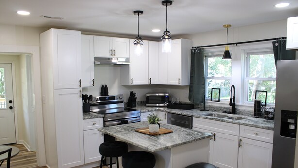 A modern kitchen with white cabinets, stainless steel appliances, a marble island, and black bar stools. - Delightful 2-bedroom house with AC in charming Easley (Easley)
