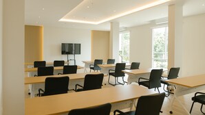 Ein Konferenzraum mit mehreren Tischen und Stühlen, großen Fenstern und einem Flachbildfernseher an der Wand.