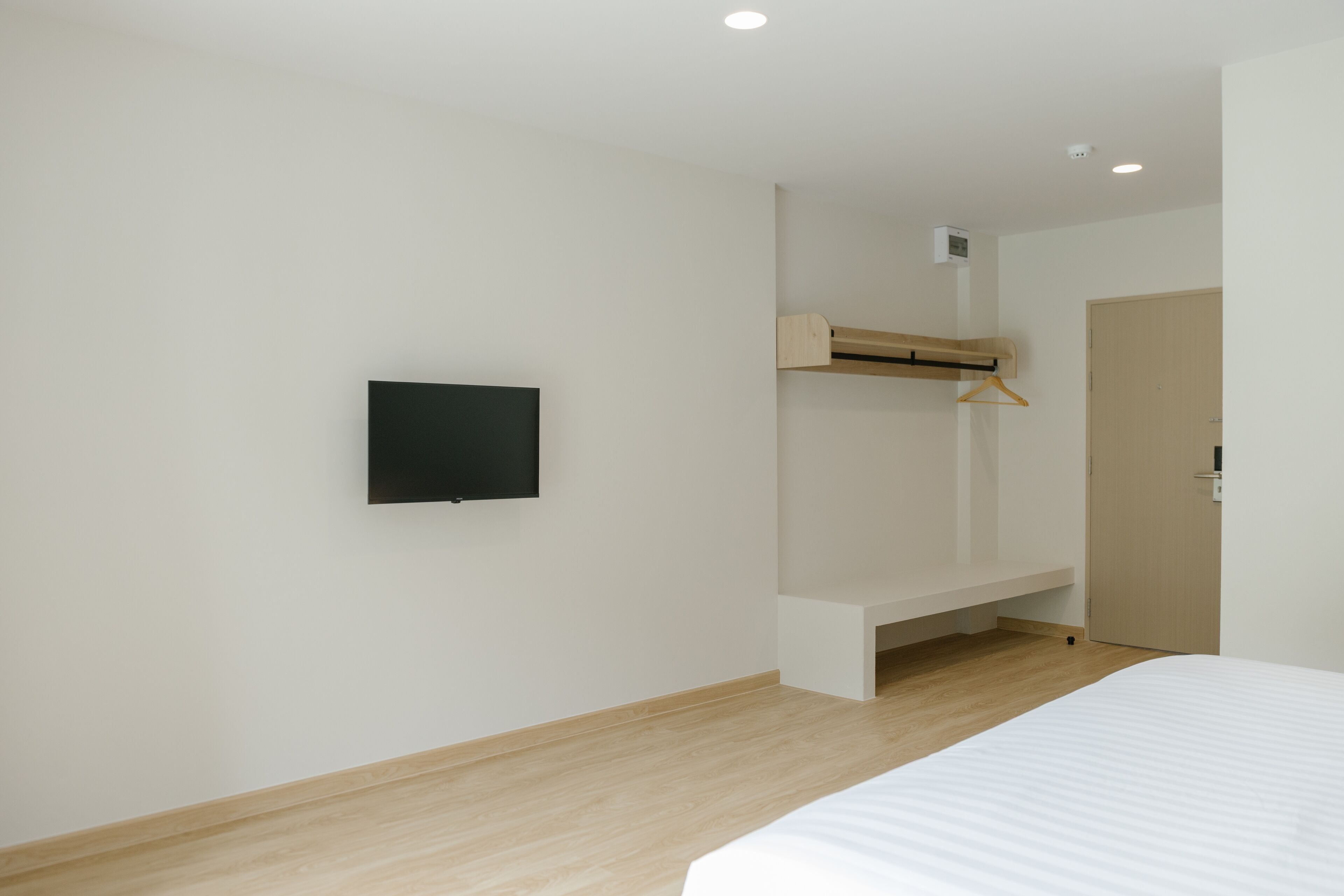 A bedroom with a bed, a TV mounted on the wall, a wooden bench, and a door.