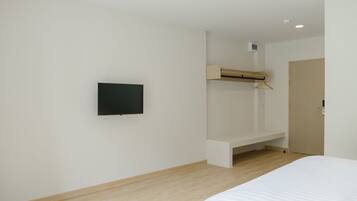 A bedroom with a bed, a TV mounted on the wall, a wooden bench, and a door.