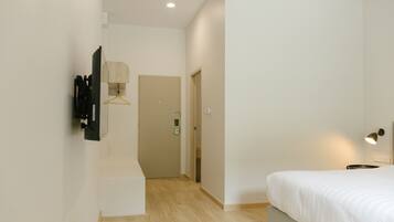 A bedroom with a bed, a hanging light, and a door leading to another room.