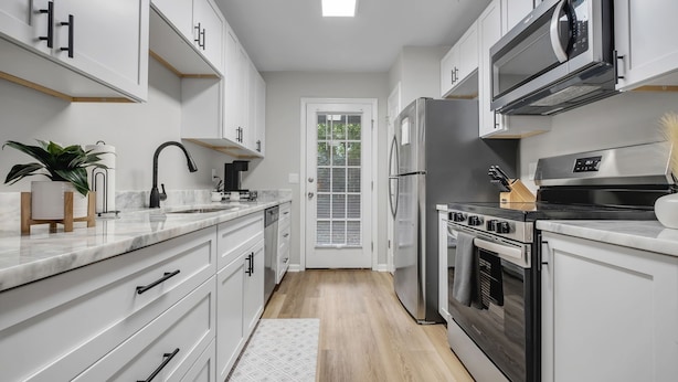 A modern kitchen with white cabinets, stainless steel appliances, and a wooden floor.