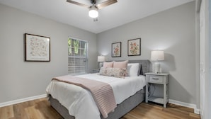 A bedroom with a bed, bedside tables, a ceiling fan, and framed artwork on the walls.