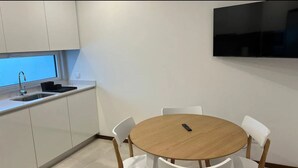 A compact kitchen with white cabinets, a sink, and a round table with chairs. - Up Sal Business (Aveiro)