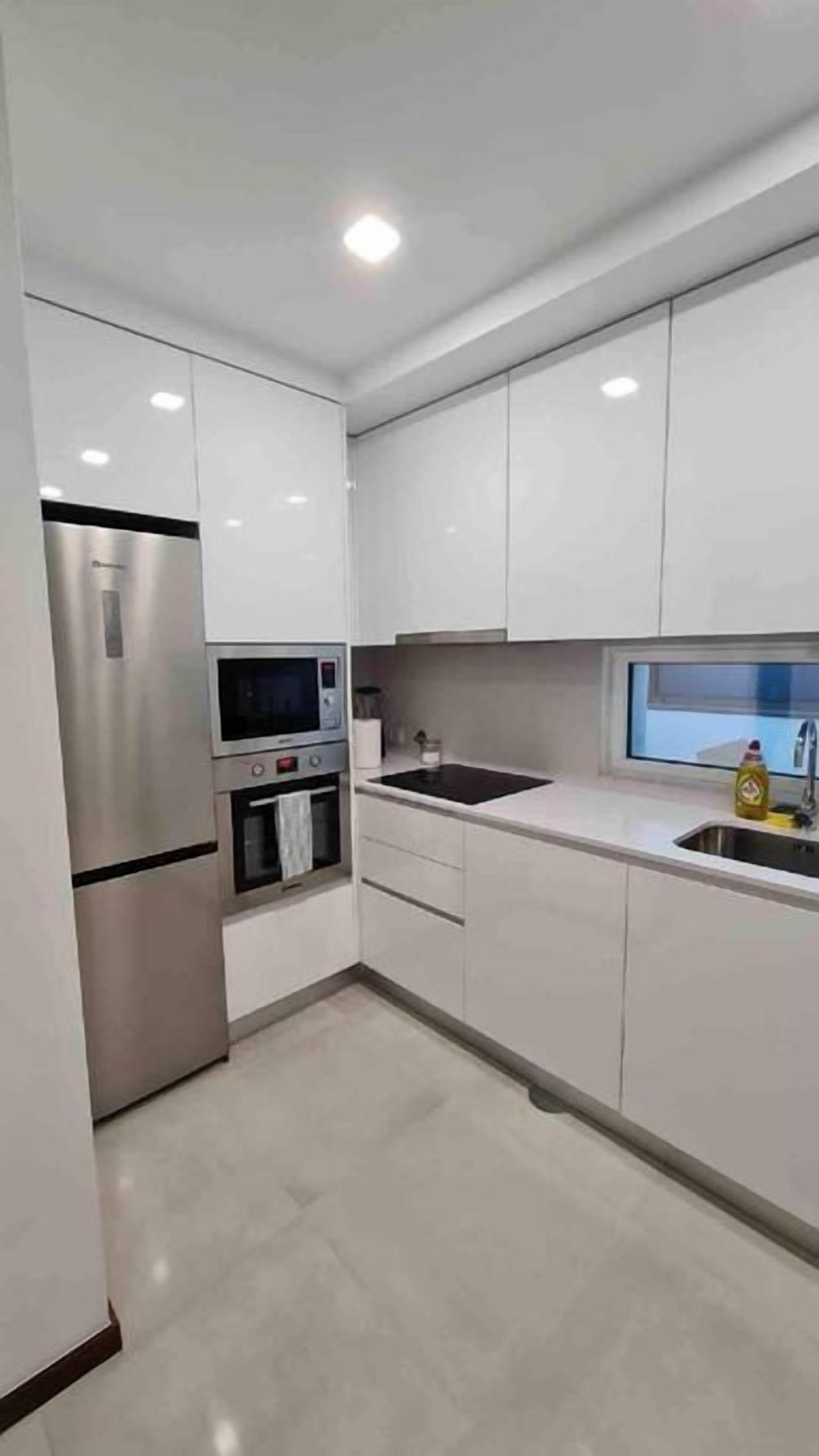 A modern kitchen with white cabinets, stainless steel appliances, and a window above the sink.