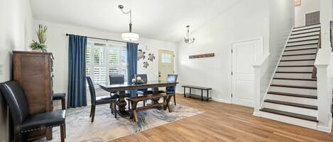 A spacious dining area with a wooden table and chairs, a chandelier, and a staircase leading to an upper level.