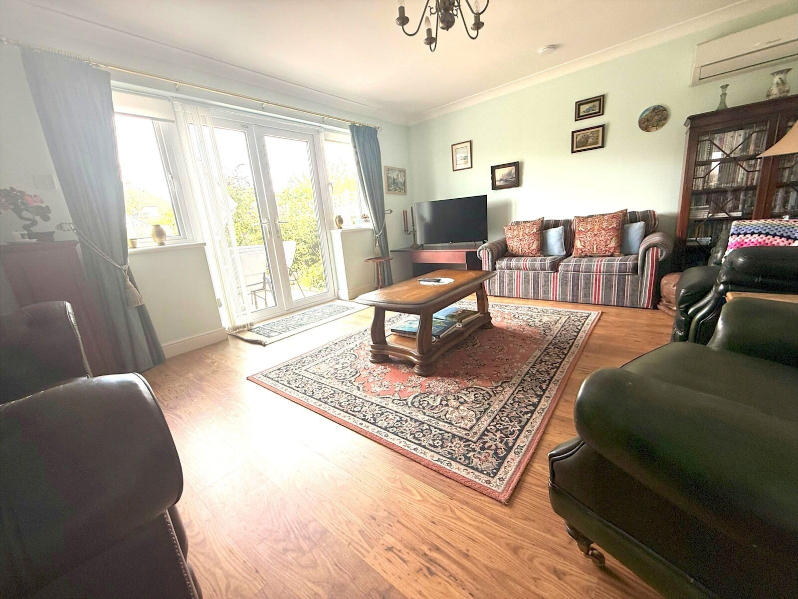 A living room with a wooden floor, a coffee table, a sofa, a television, and a bookshelf.