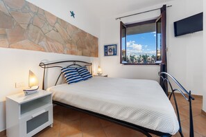 Una camera da letto con un letto, comodini, una parete in pietra, una finestra e una TV a schermo piatto.