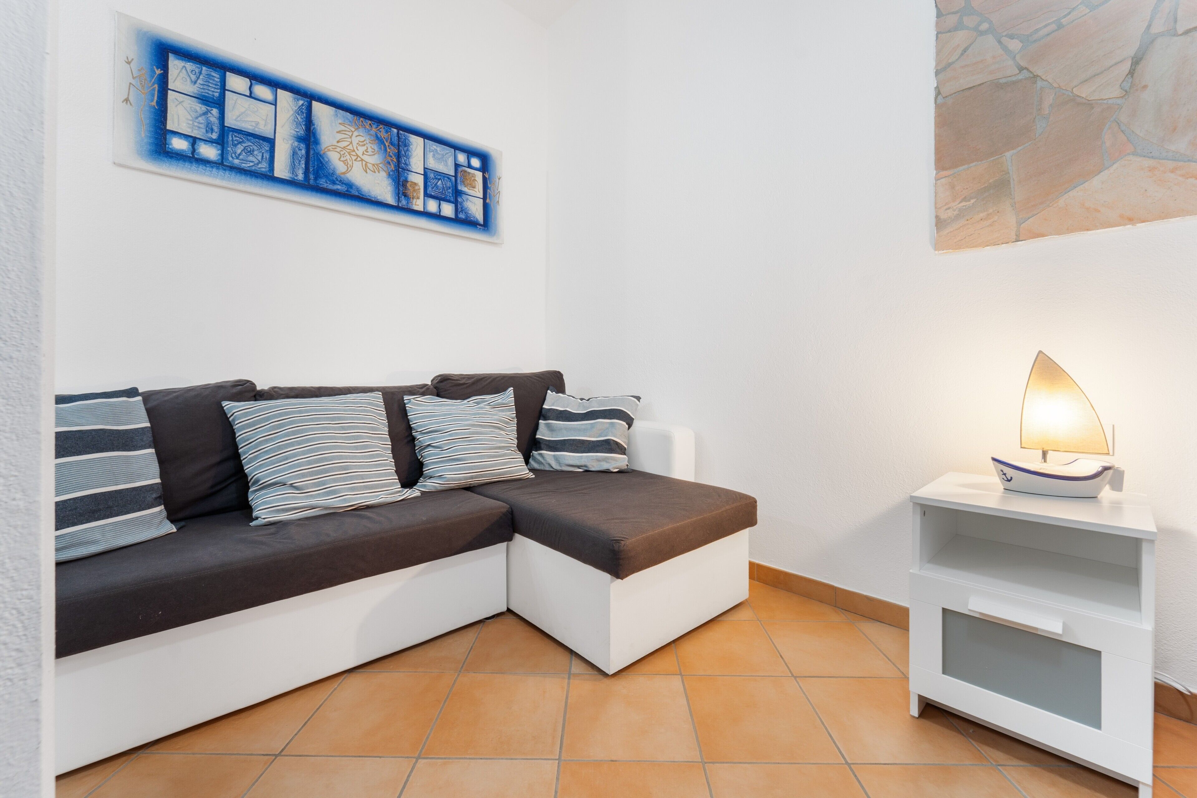 Ein modernes Wohnzimmer mit einer Eckcouch, einem Beistelltisch mit Lampe und einem Wandbild.