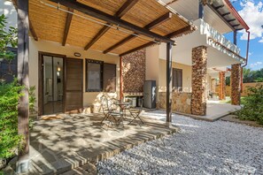 Eine überdachte Terrasse im Freien mit Steinpfeilern, einer Steinmauer und einem Tisch mit Stühlen.