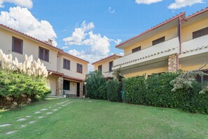 Un edificio a due piani con un giardino antistante, colonne in pietra e un cielo azzurro intenso.