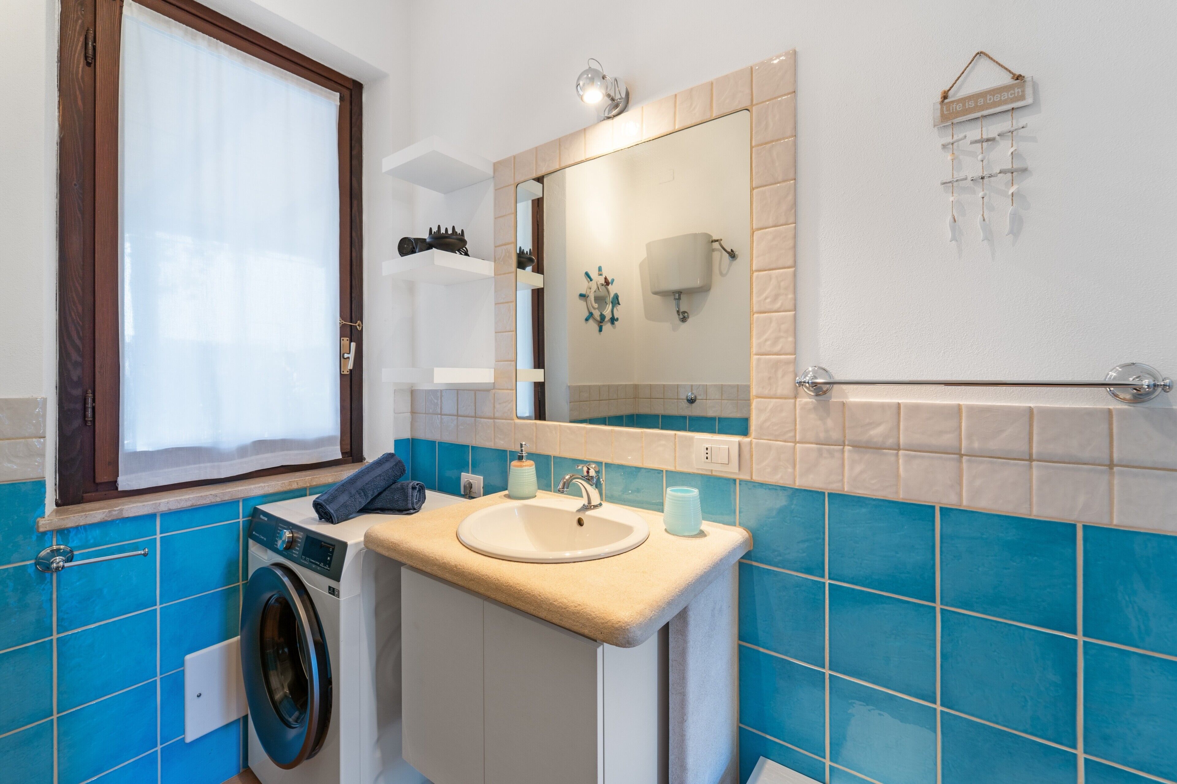 A bathroom with a washing machine, sink, mirror, towel rack, and blue-tiled walls.