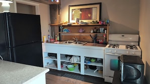 Une cuisine de taille réduite avec un réfrigérateur noir, une cuisinière blanche et des étagères en bois au-dessus de l’évier.