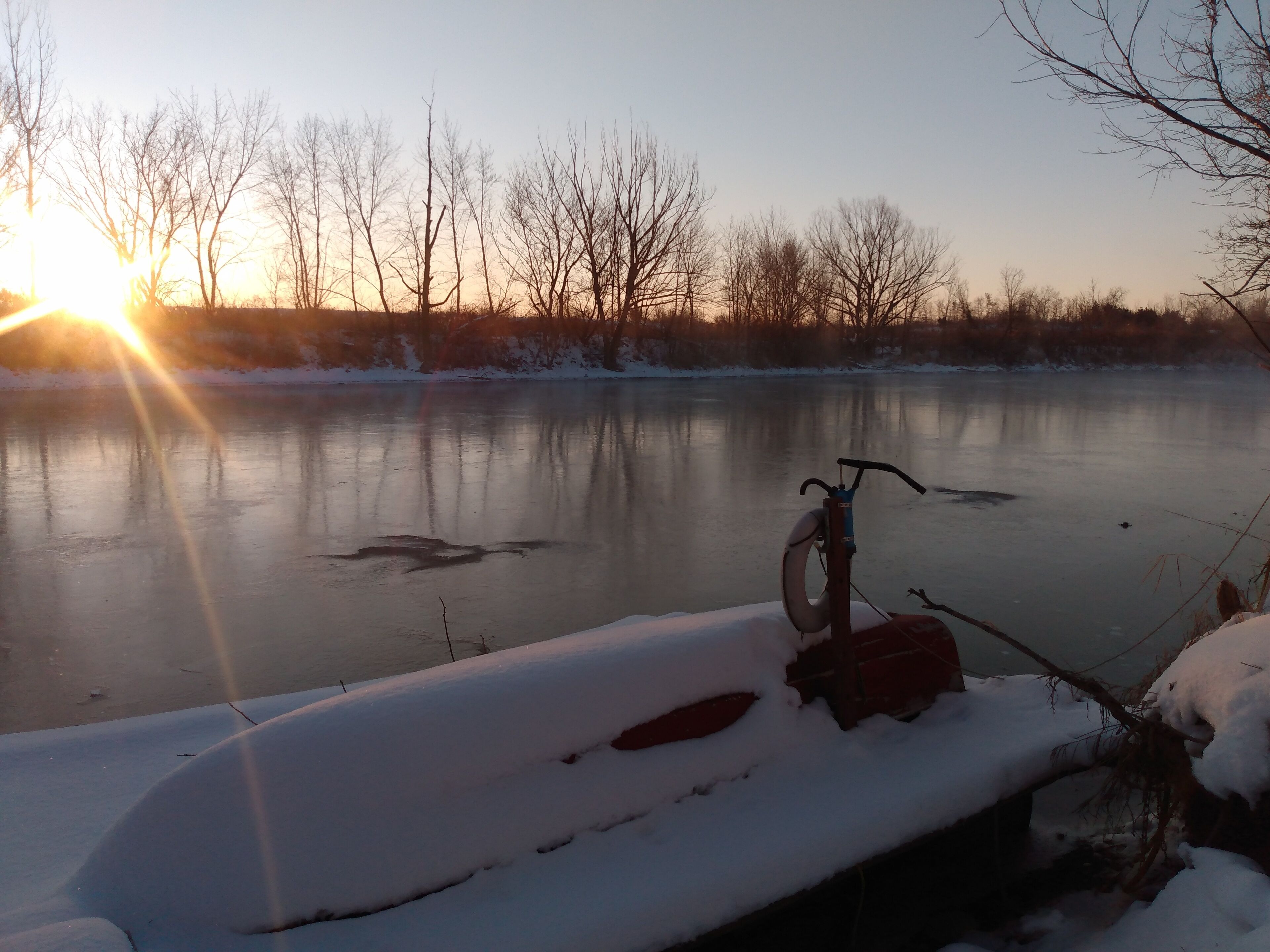 A bicycle parked on a snow-covered path beside a frozen body of water with trees in the background.