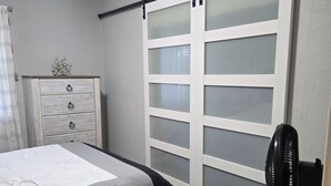 Un dormitorio con cama, cómoda, reloj y puerta corredera.