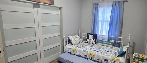 A bedroom with a bed, a dresser, a painting, a window with curtains, and a sign on the wall.