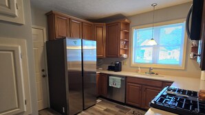 Una cocina funcional con armarios de madera, un refrigerador de acero inoxidable, una estufa y un ventanal con persianas.