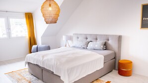 Ein modernes Schlafzimmer mit einem großen Bett, einem Nachttisch, einer Lampe und einem Fenster mit Vorhängen.