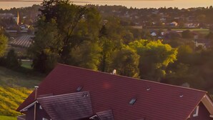 Ein Wohngebiet mit einem markanten Haus mit rotem Dach, einem sichtbaren Kirchturm und einem Gewässer im Hintergrund.