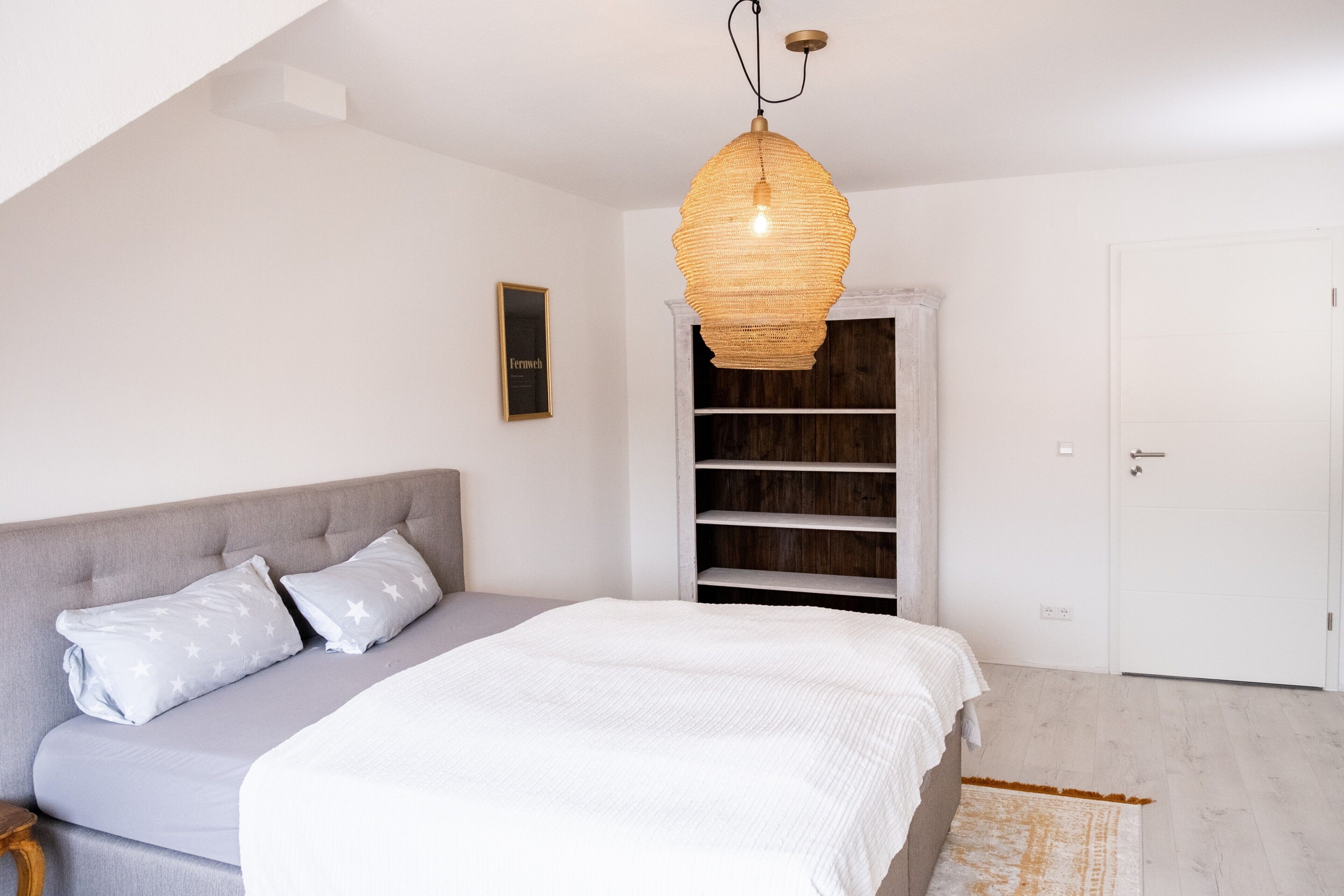 Une chambre à coucher avec un lit, un canapé gris, une porte blanche et une armoire en bois.