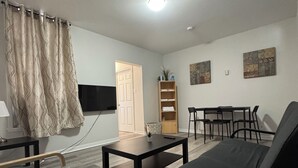 A living room with a sofa, a coffee table, a TV, a bookshelf, and a door. - Serenity Suite - 2Br (Cornwall)