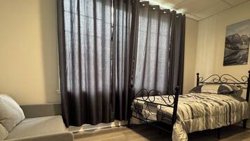 Ein Schlafzimmer mit einem Bett, einem Sessel und einem großen Fenster mit Vorhängen.