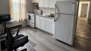 A compact kitchen with white cabinets, a refrigerator, a microwave, and a stove. There is a dining table with chairs and a window with curtains. - Serenity Suite - 2Br (Cornwall)