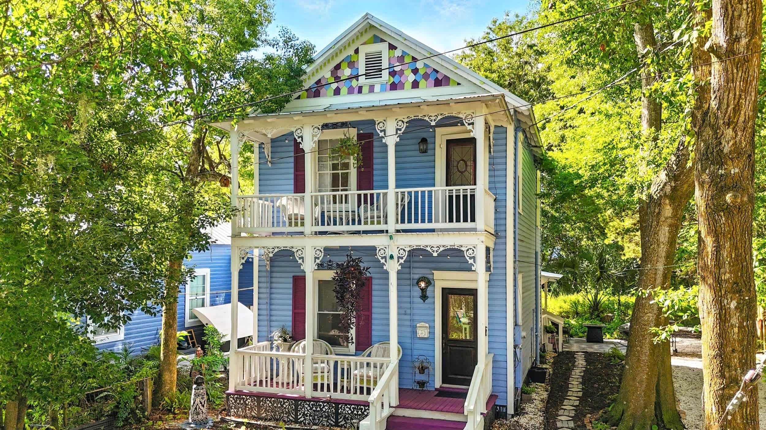 Una casa de dos pisos con un balcón, rodeada de árboles.