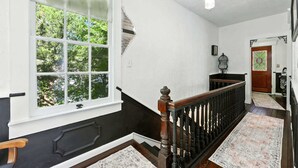 Una escalera con barandilla de madera y balaustradas negras, que conduce a una puerta con un vitral.