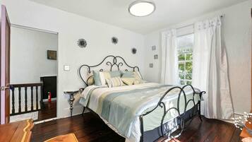 Un dormitorio con cama, piso de madera, ventana con cortinas y una puerta.