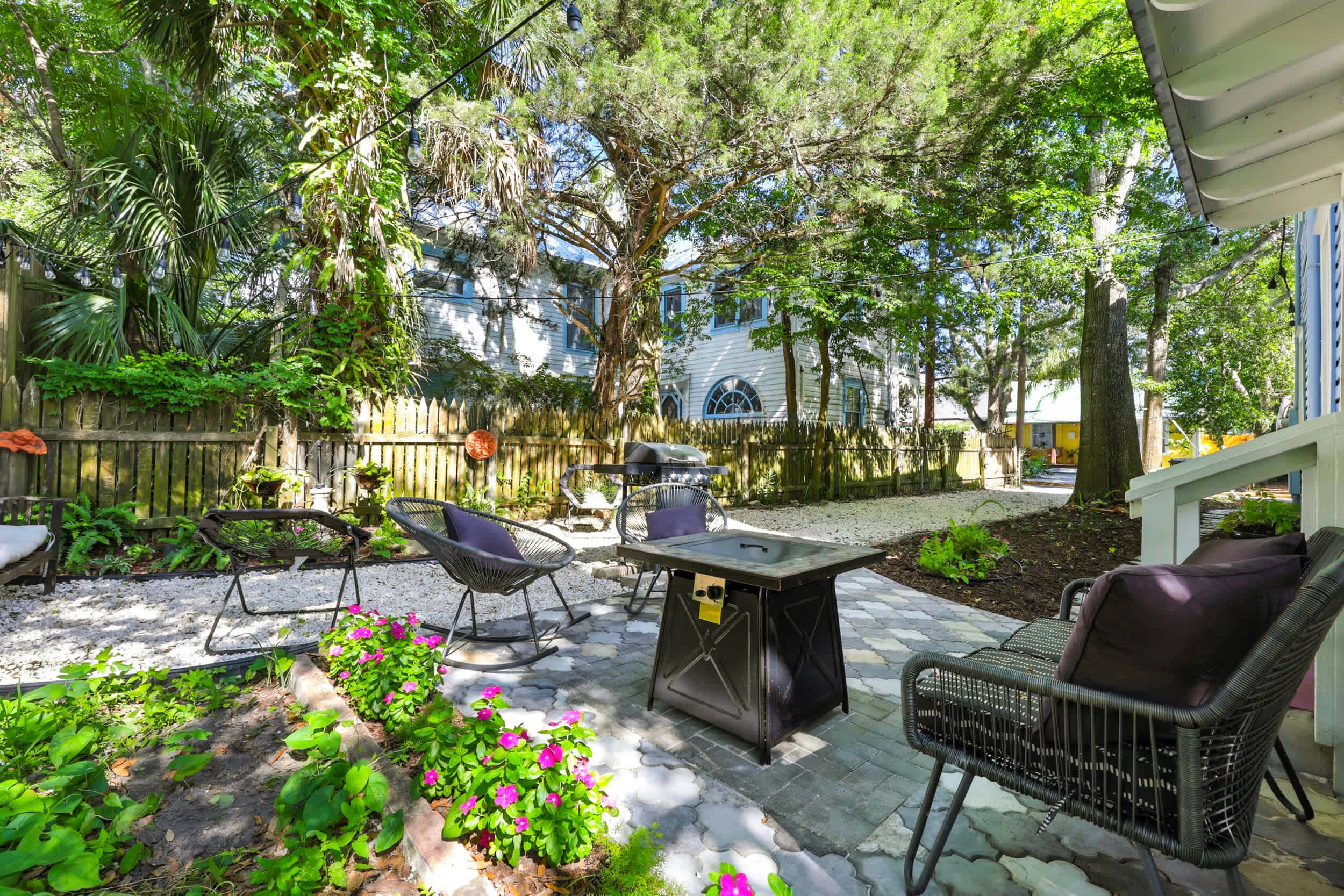 An outdoor patio with a table and chairs, surrounded by greenery and a wooden fence.