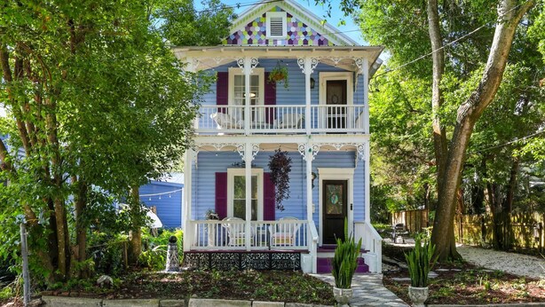 Una casa de dos pisos con balcón, rodeada de árboles y un jardín.