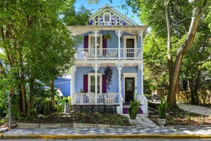 Une maison à deux étages avec un balcon, entourée d’arbres et d’un jardin.