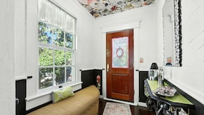 Una habitación acogedora con un sofá, una puerta de madera con un vitral, una mesita con una tetera y un espejo en la pared.